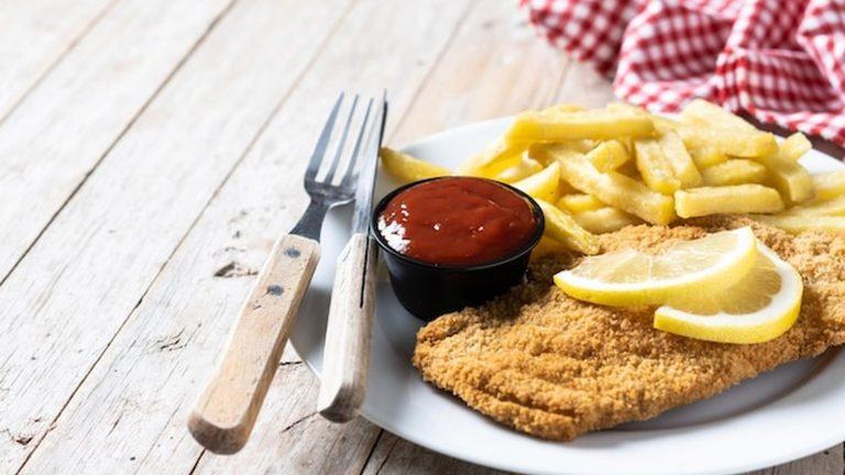 שניצל וינאי טירולי מסורתי עם תפוחי אדמה מטוגנים על שולחן עץ - מסעדות קיצביהל וזעפלד